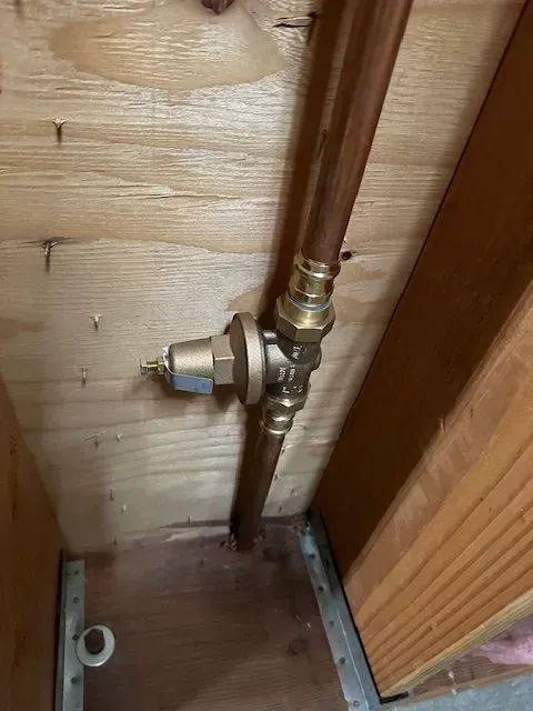 Copper pipes and a brass fitting with a valve in a wooden enclosure.