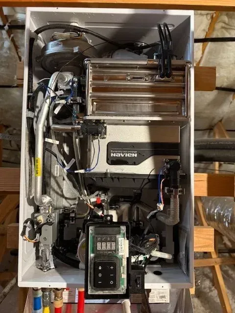 Open view of a white wall-mounted Navien tankless water heater, showing internal components and control panel. The setting appears to be an unfinished basement.