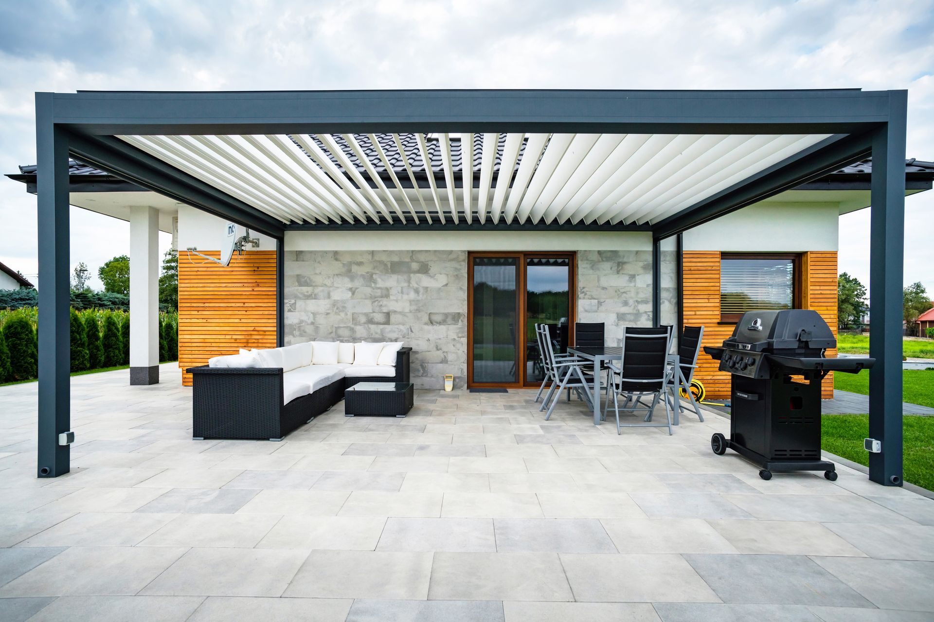 Un patio con pergolato e griglia davanti a una casa.