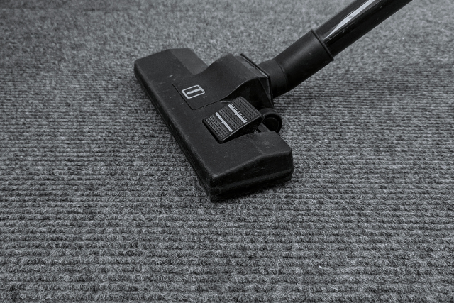 A black vacuum cleaner attachment resting on a gray, ribbed carpet.