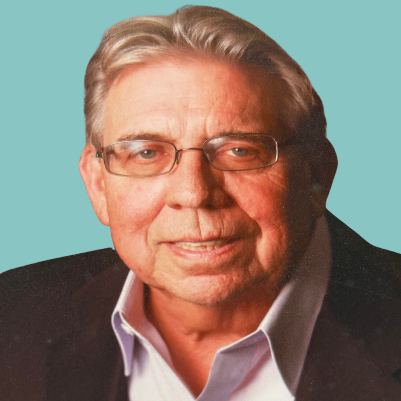 Man with glasses, wearing a white shirt and dark jacket, smiling, teal background.