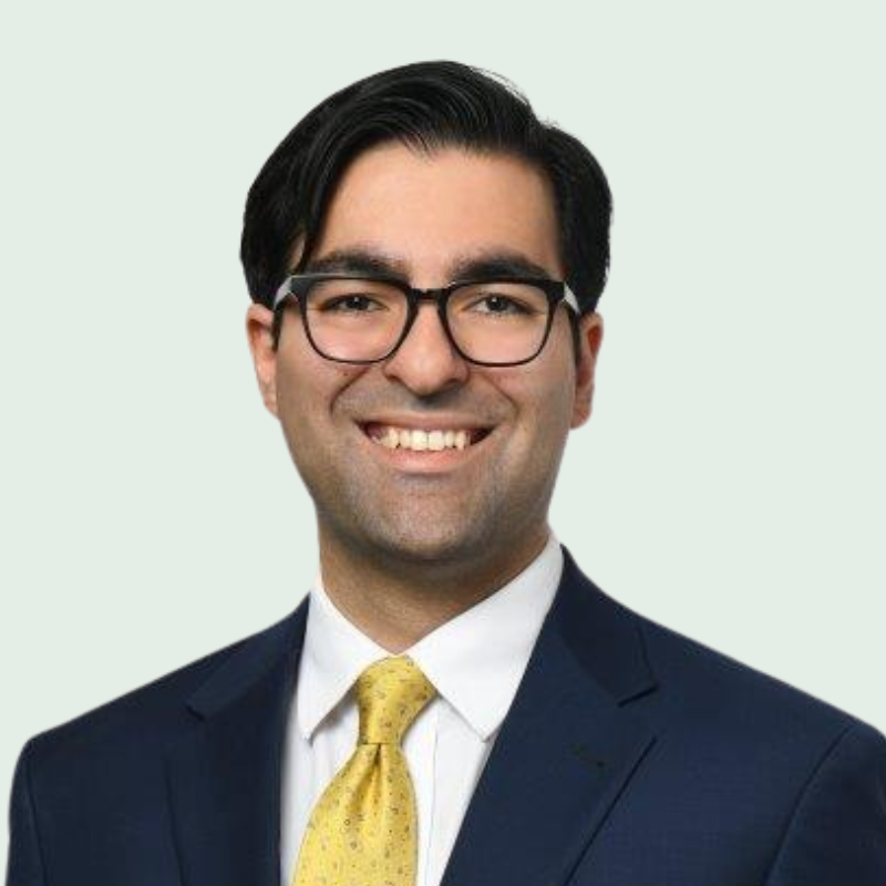 Man wearing glasses and a yellow tie, smiles in a dark suit.