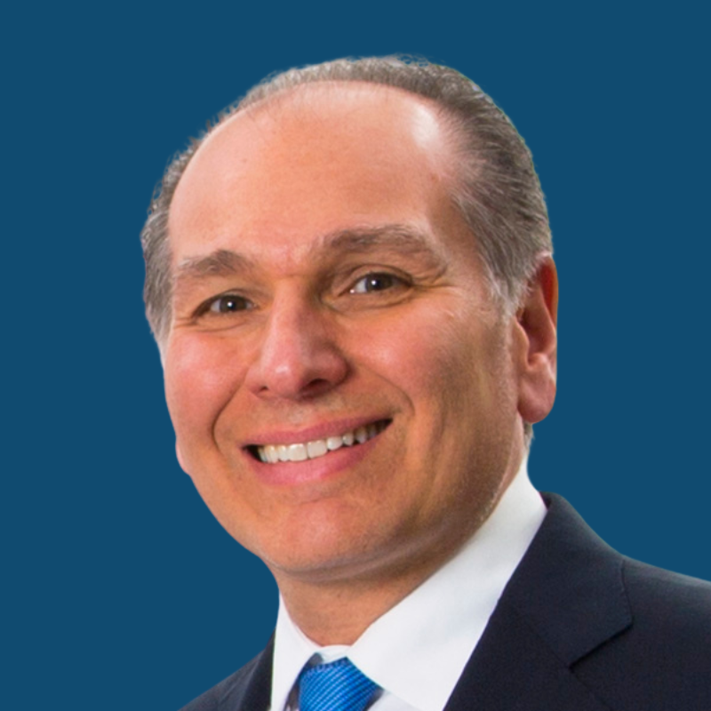 Man in suit smiling, against a blue background.