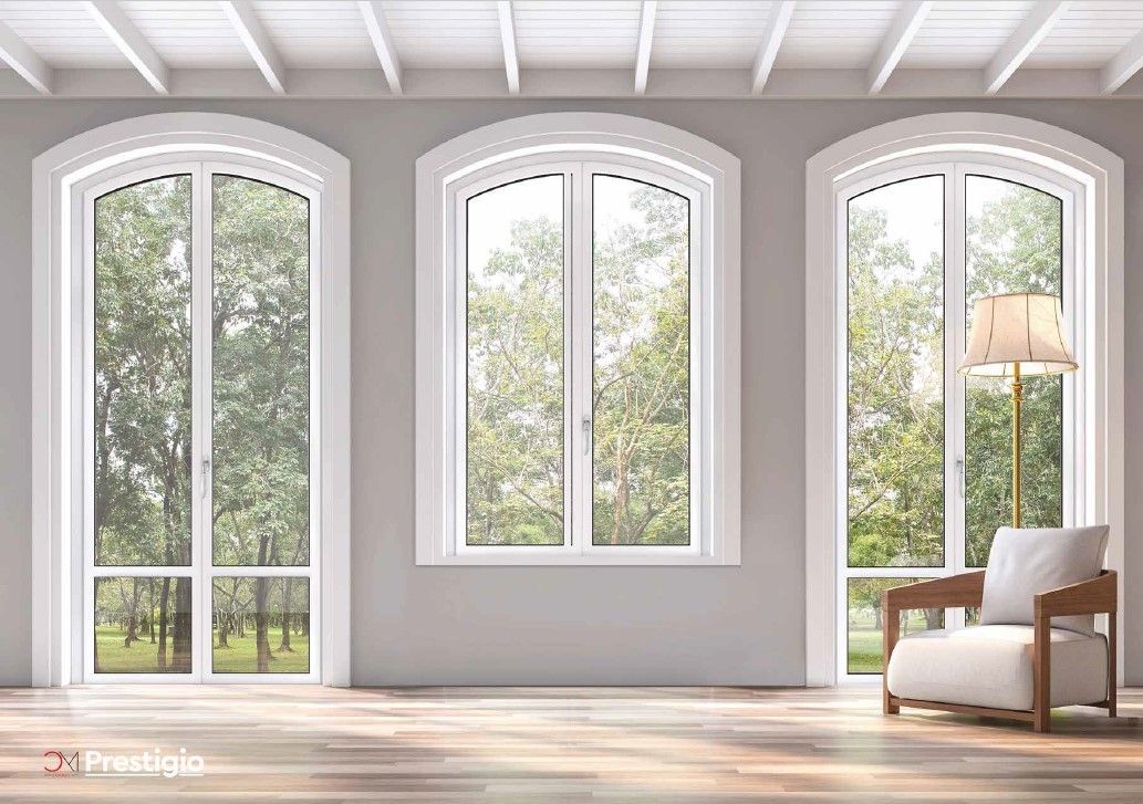 Tre finestre ad arco con cornice bianca con vista sugli alberi, una poltrona e una lampada su una parete grigia.