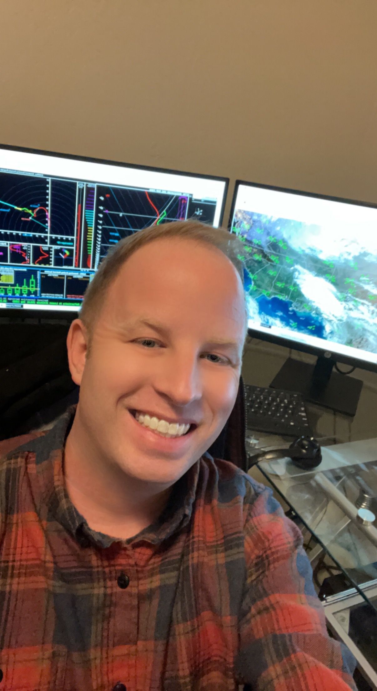 Jay Roberts smiles, in front of two computer screens displaying weather data.