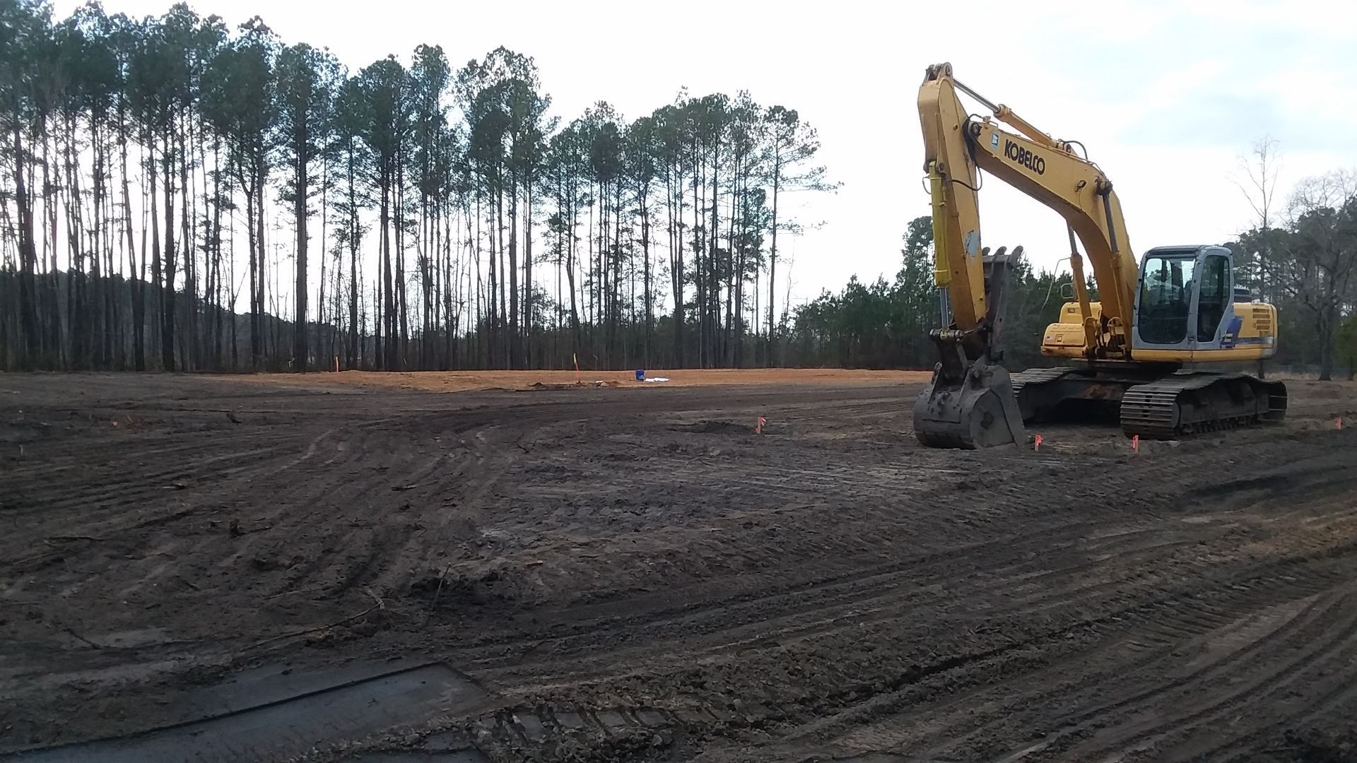 A yellow excavator is working in a field with trees in the background