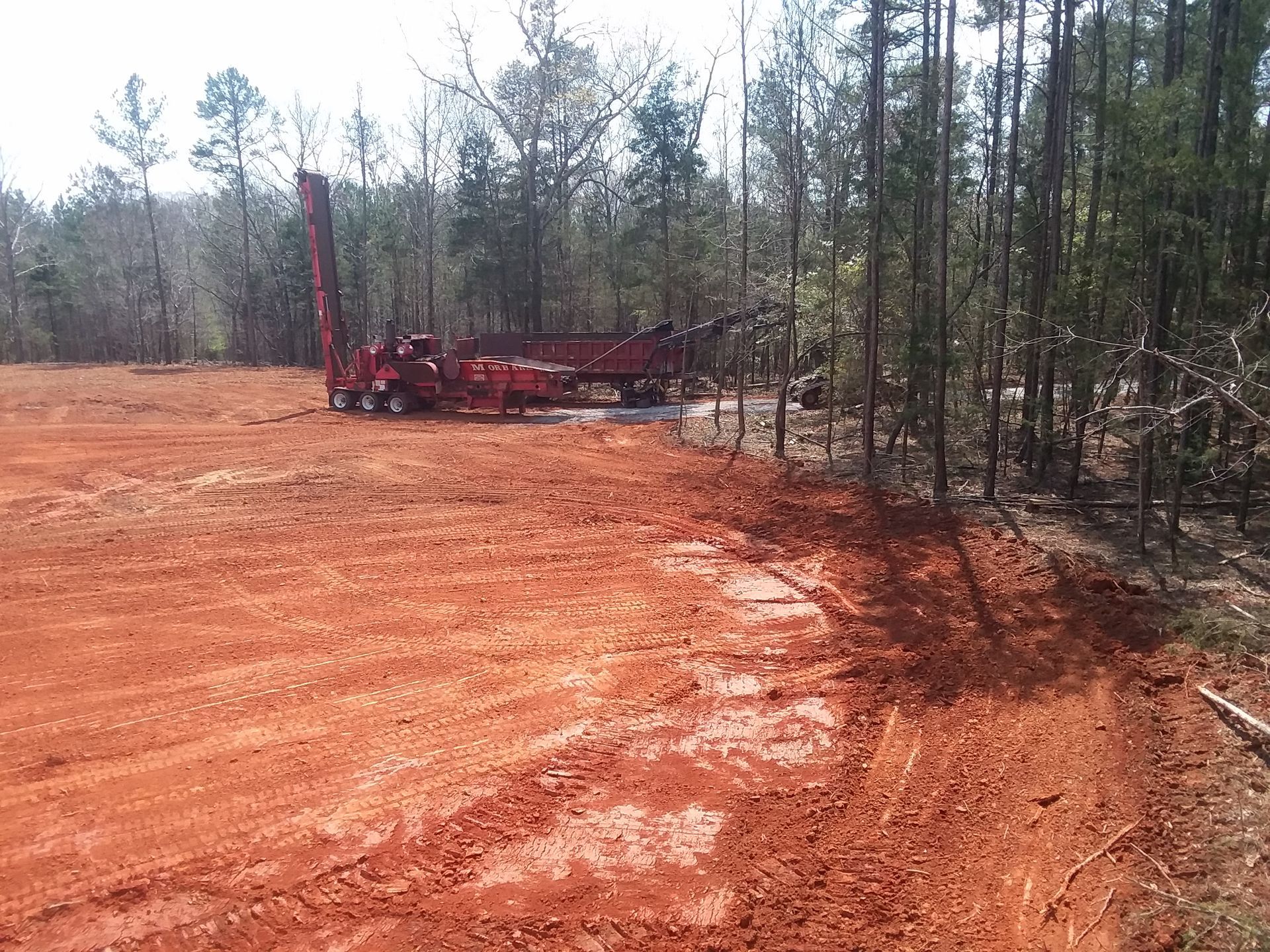 A red crane is sitting in the middle of a dirt field.