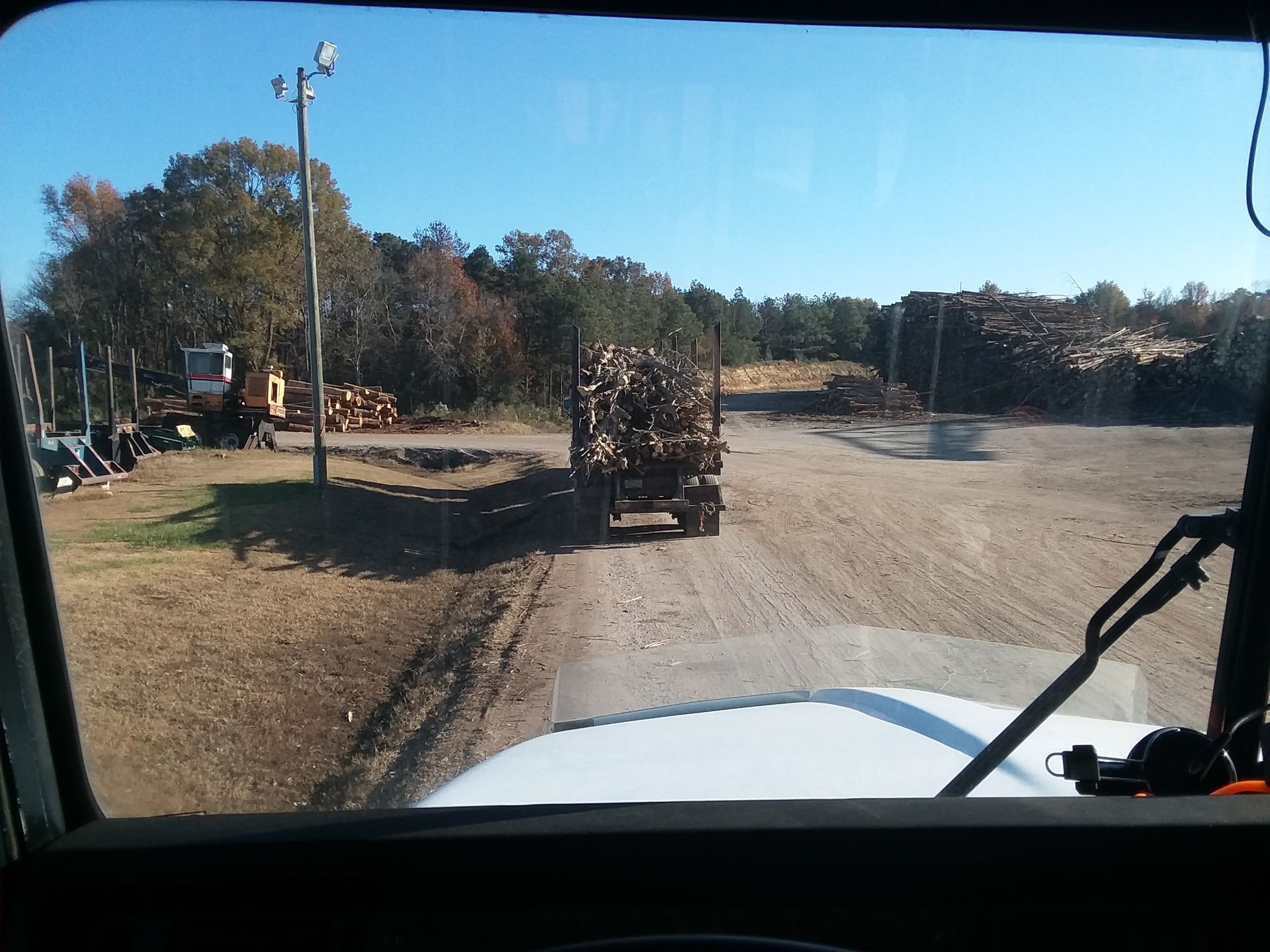 A truck carrying logs is driving down a dirt road