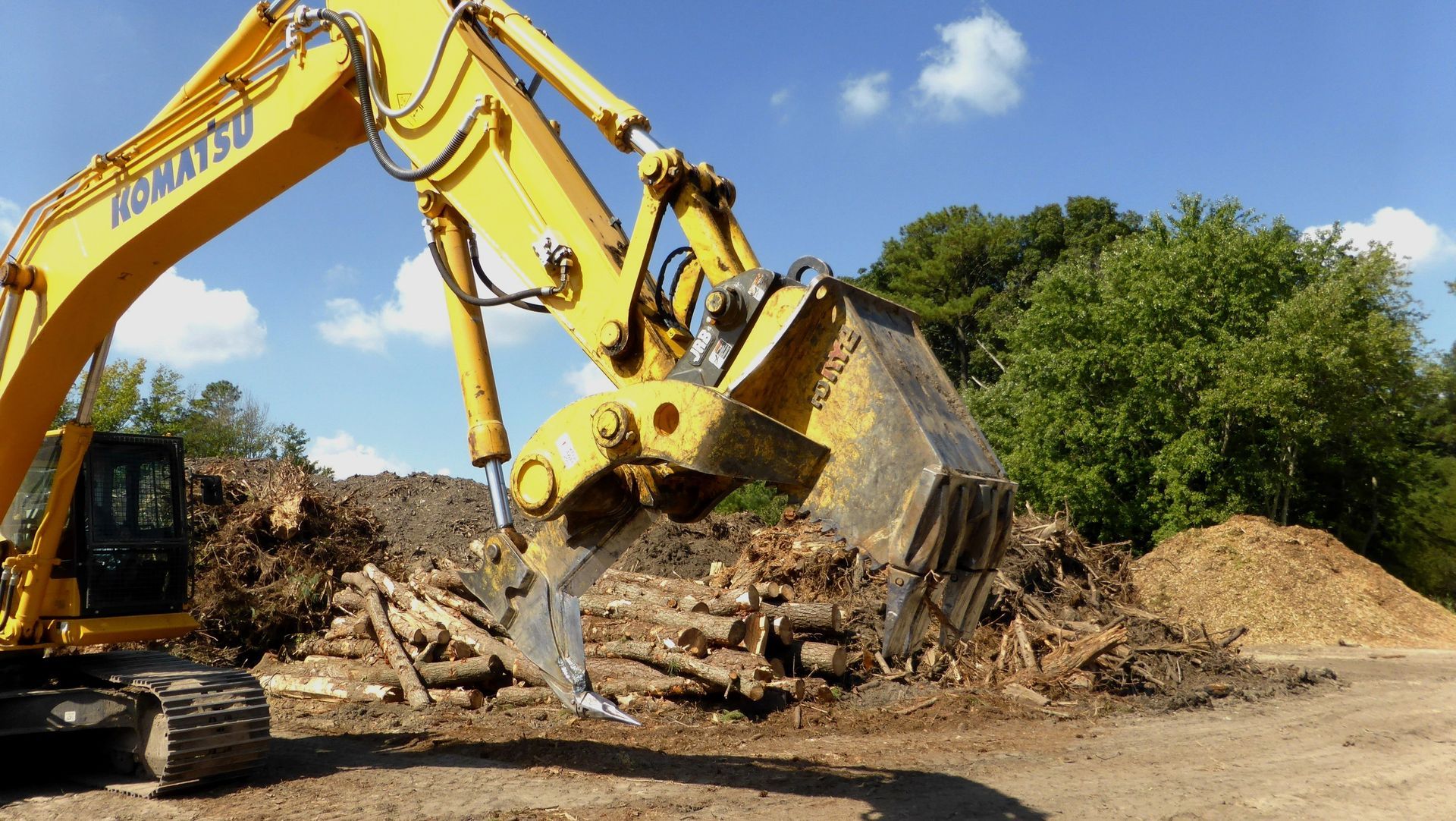 A yellow excavator is digging in a pile of wood.