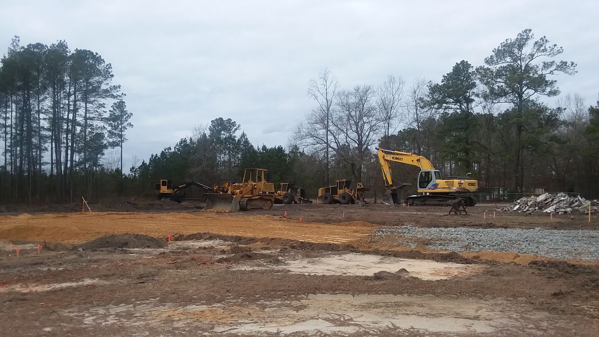 A group of construction vehicles are working on a dirt field.