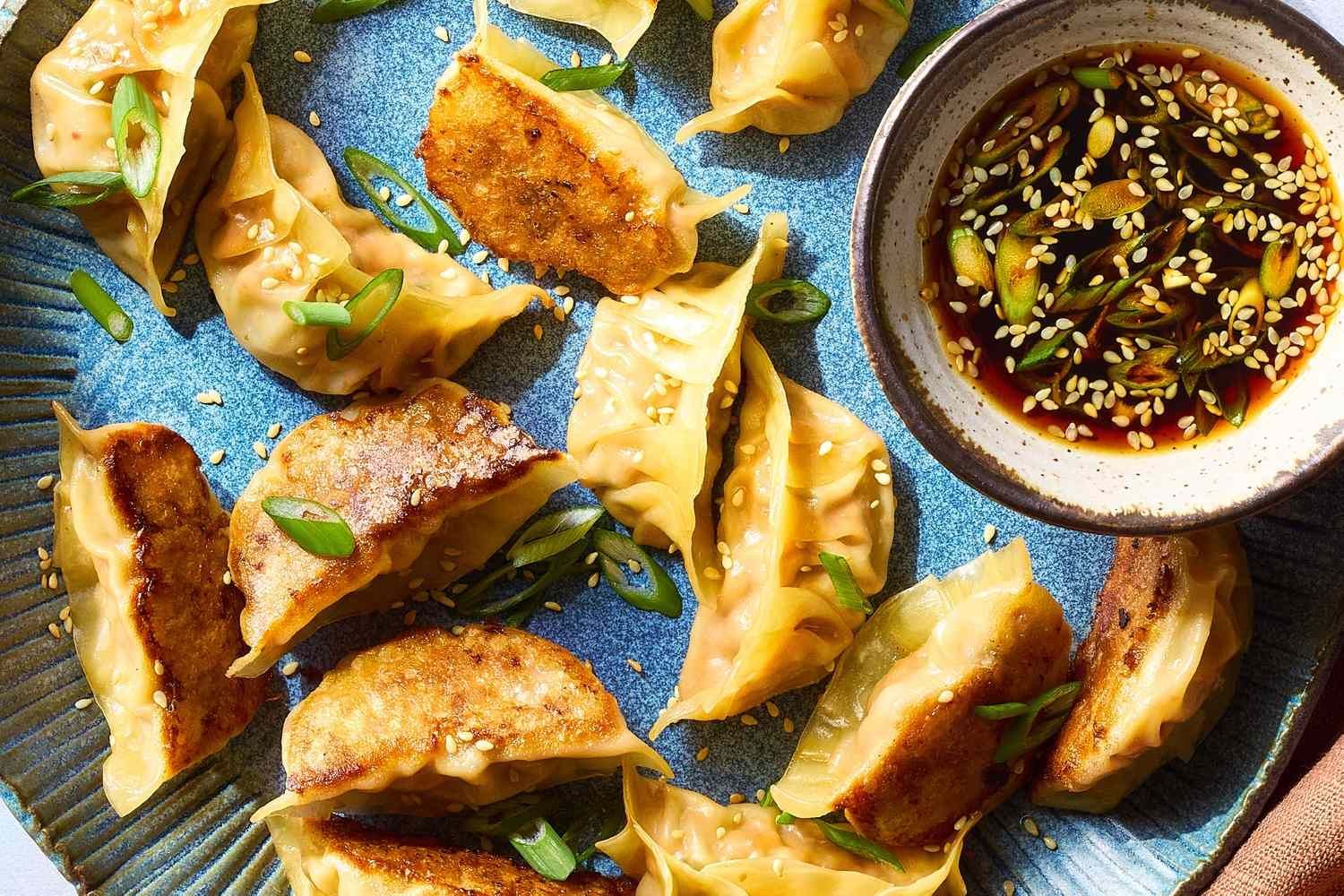 Pan-fried dumplings with sesame seeds and scallion garnish, served with dipping sauce.