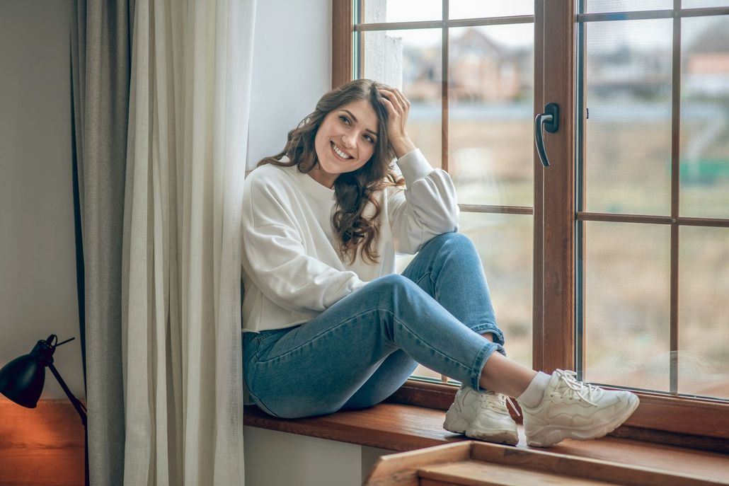 A woman is sitting on a window sill looking out the window.