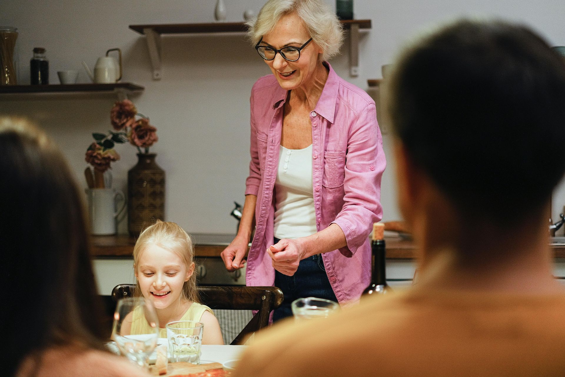 A woman in a pink shirt is standing in front of a family sitting at a table.