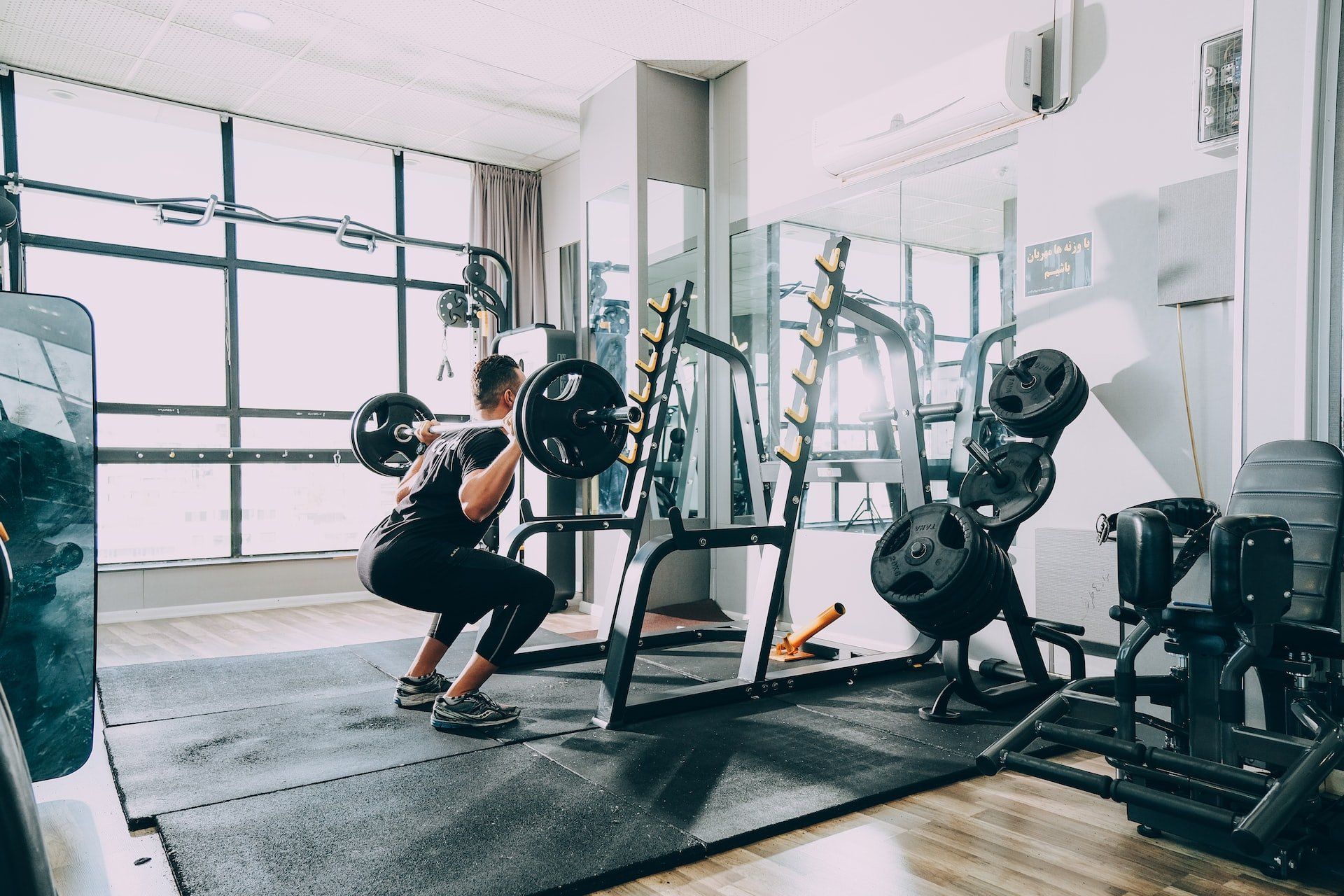 A man is squatting with a barbell in a gym.