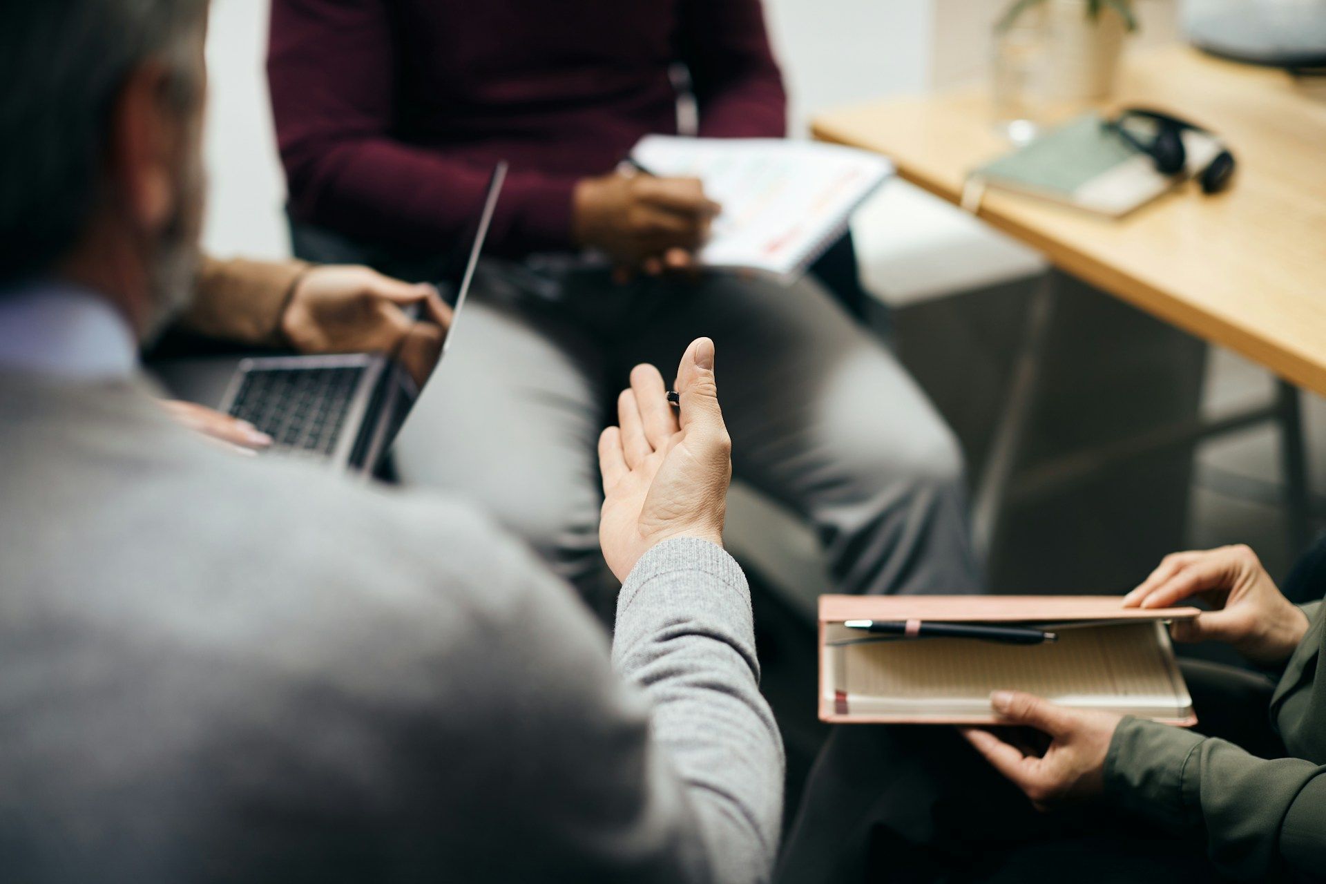 Group discussion in a meeting room, with hands gesturing over a table and notebooks visible.
