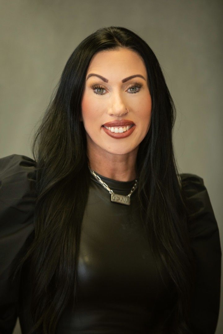 Portrait of a smiling woman with long black hair, wearing a black top against a neutral background