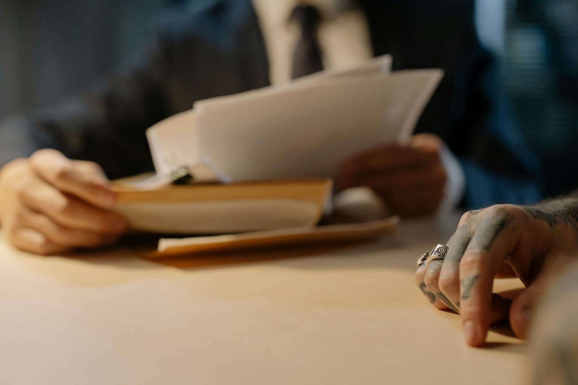 Hands sorting papers on a desk, with a book and stack of documents in the background