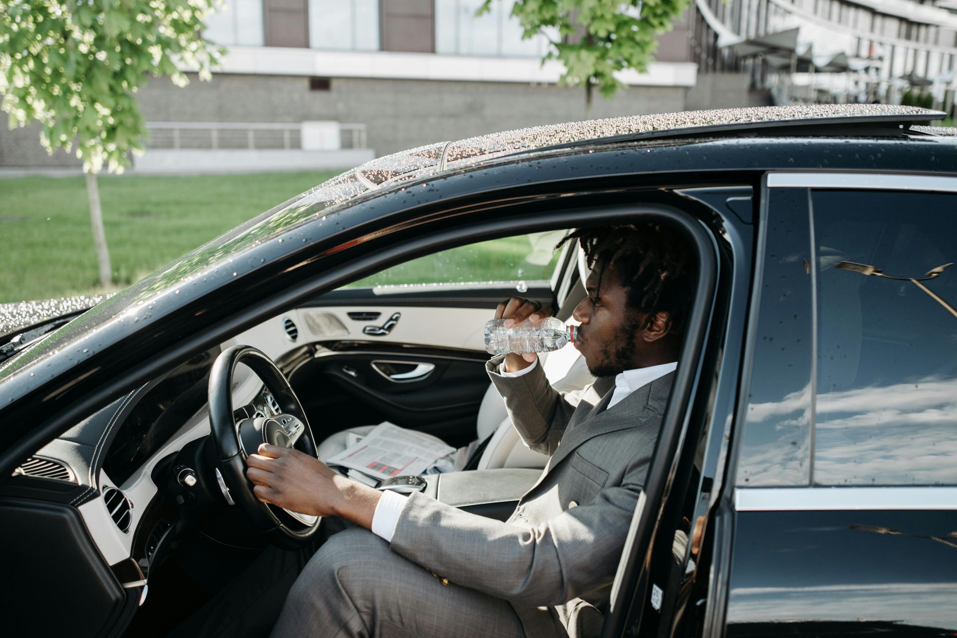 A man in a suit is sitting in a car drinking water.