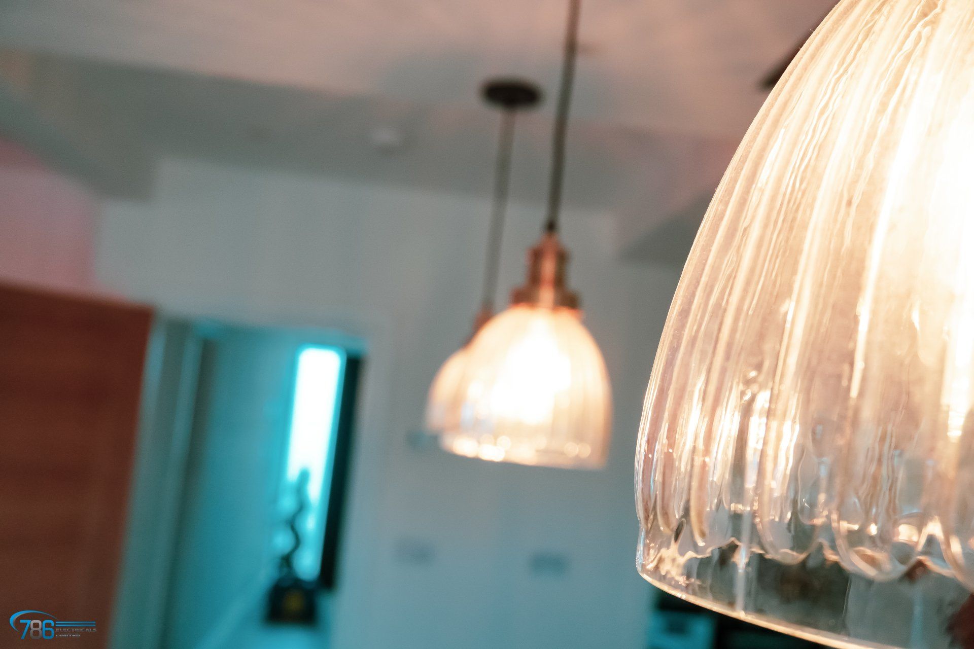Three pendant lights hanging from a ceiling, with a blurred kitchen in the background.