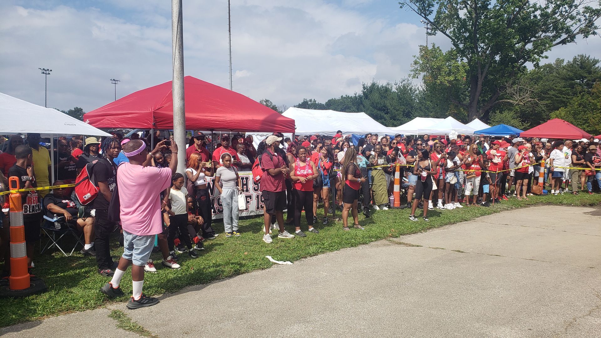 Crowd of people at an outdoor event under red and white tents, with many wearing red.