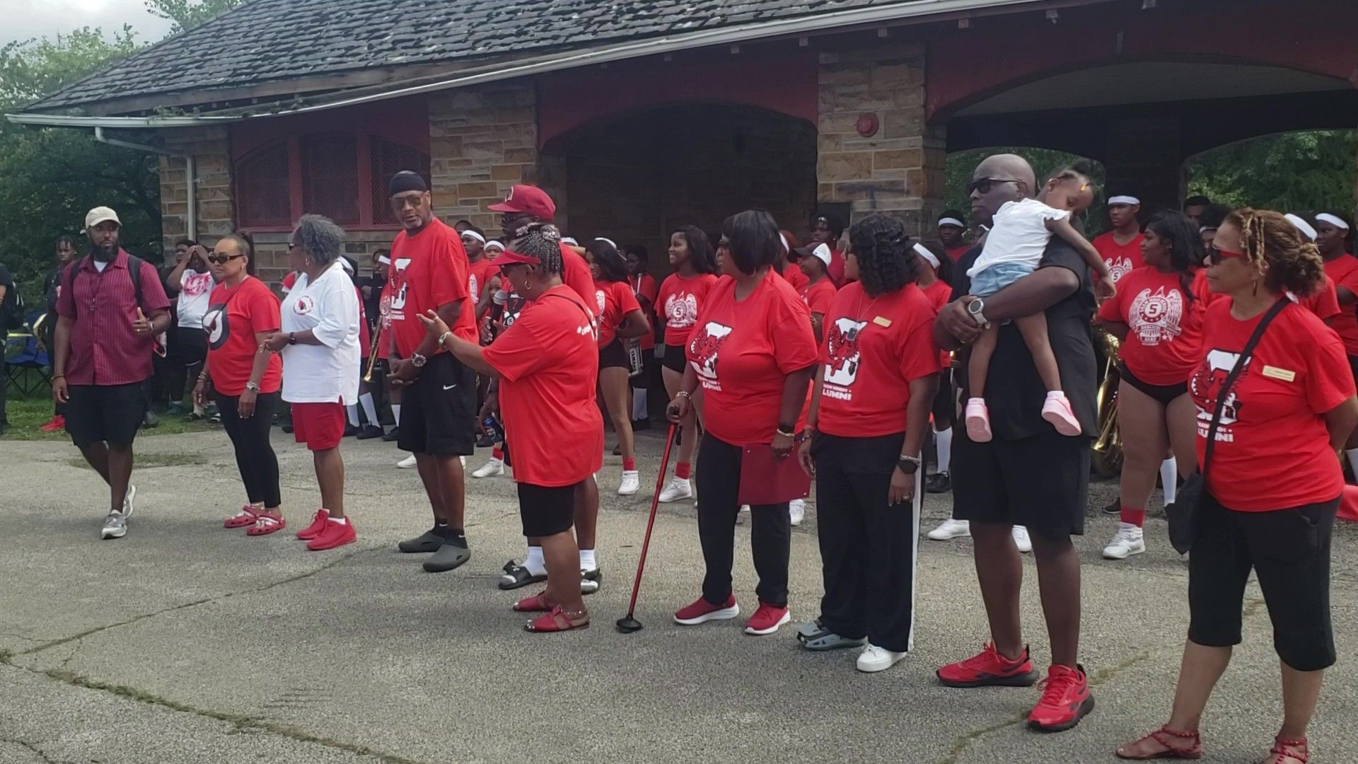 Group of people in red shirts and shoes gather in front of a park building.