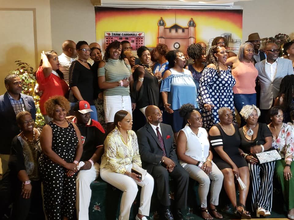 Group of diverse people at an event, smiling. Some are seated and some standing in front of a backdrop.