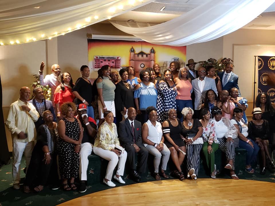 Group photo of many Black people at an event with a stage backdrop and decorative lights.