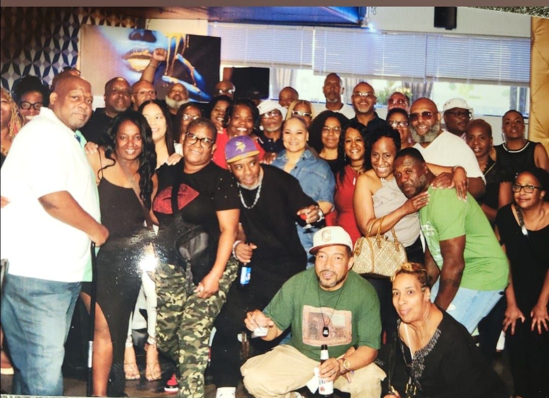 Large group of diverse people smiling for the camera at an indoor gathering, some holding drinks.