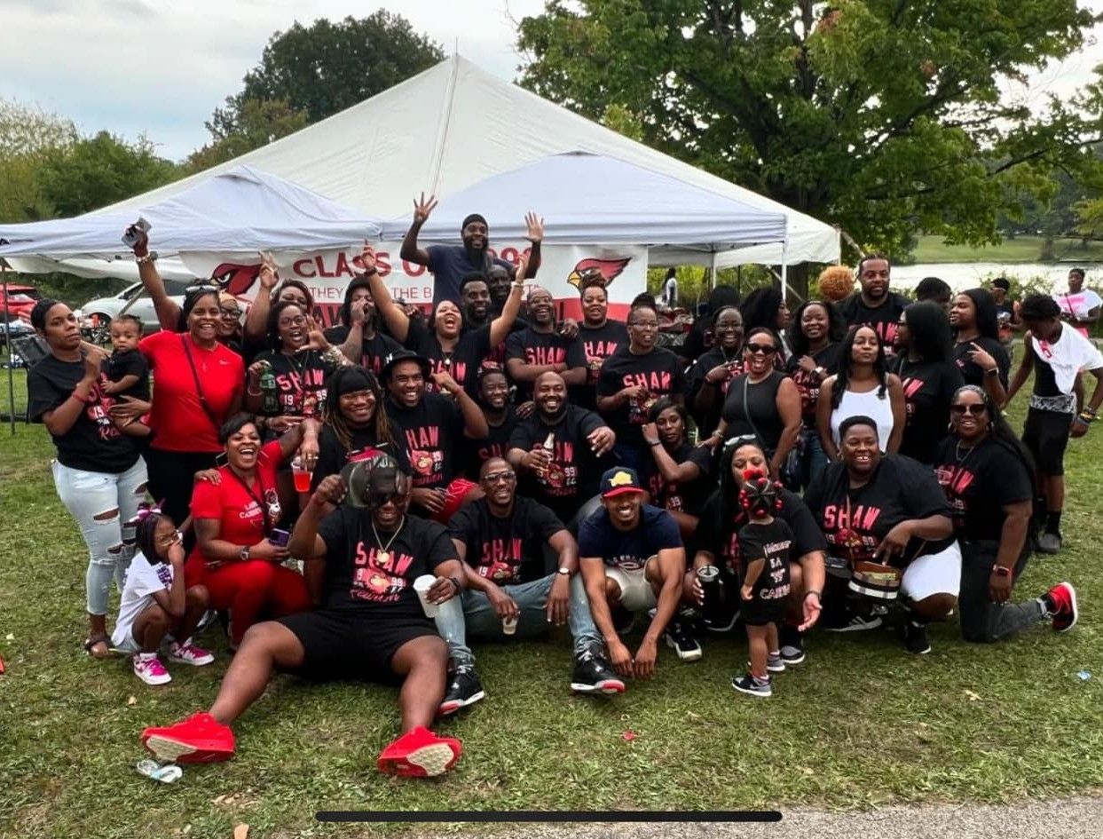 A large group of people in red and black attire pose for a photo under a white tent outdoors.