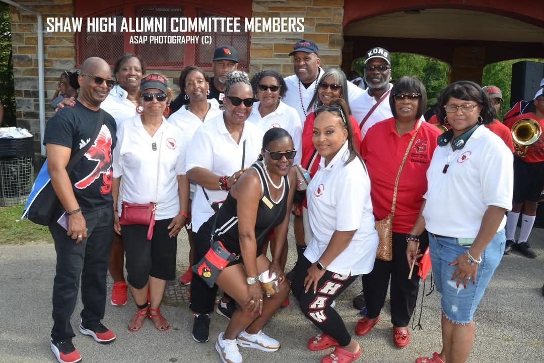 Group of Shaw High Alumni wearing red & white, posing in front of building with sign.