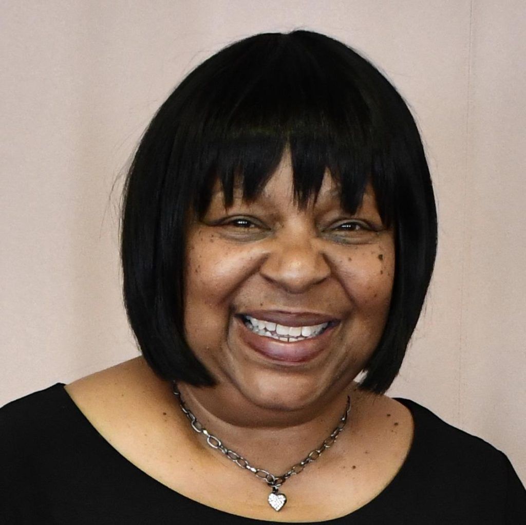 Smiling woman with short black hair, wearing a black top and necklace.