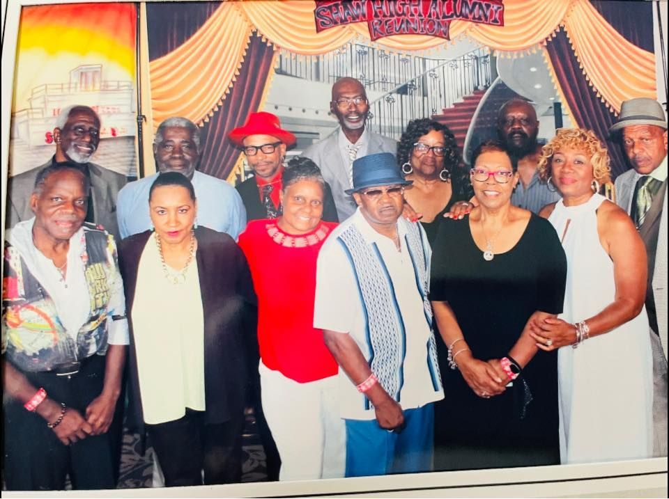 Group photo: diverse people, celebratory attire, in front of a draped stage backdrop with red, orange, and brown tones.