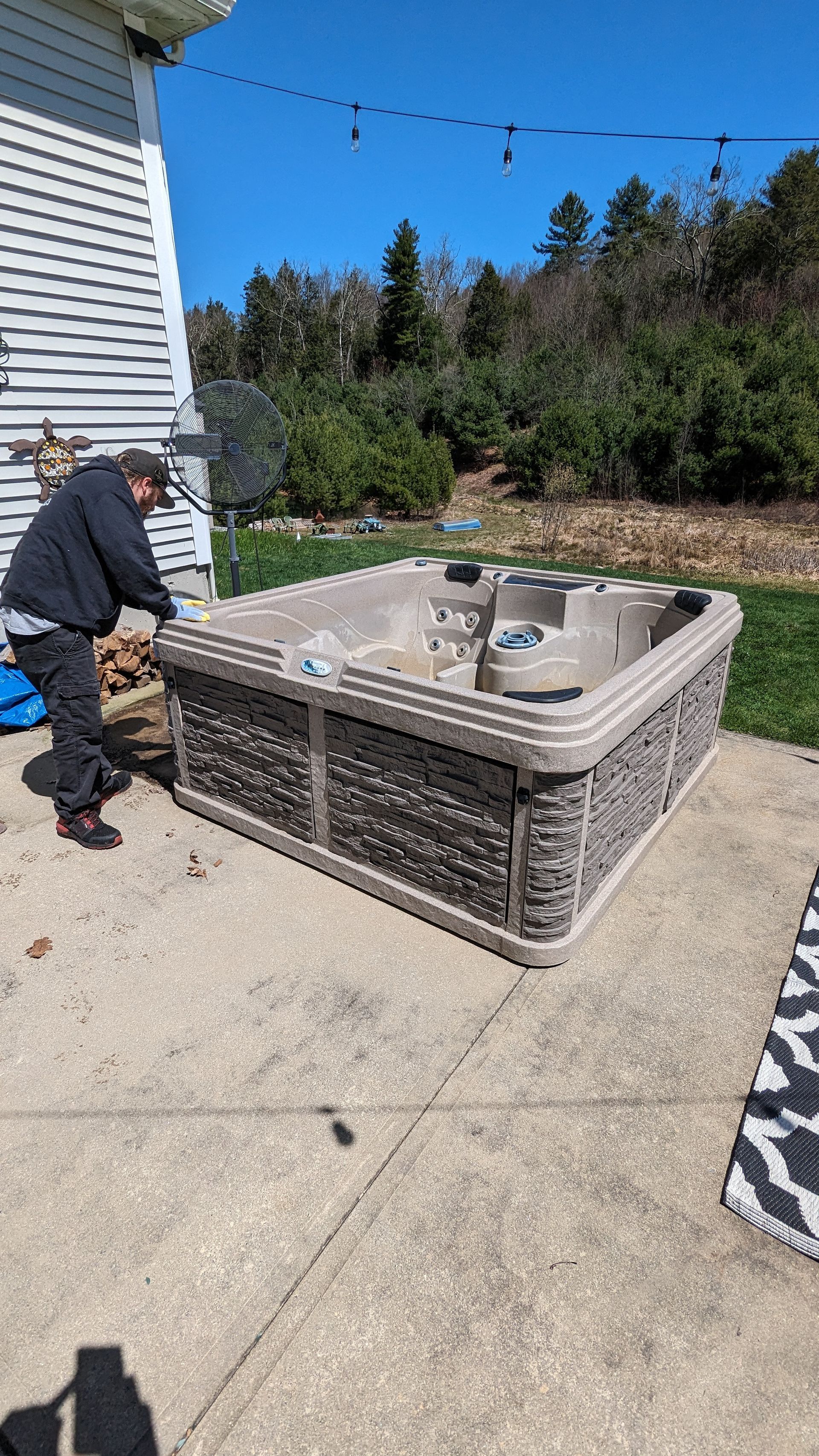 Man near a hot tub on a concrete patio, next to a white house, on a sunny day.