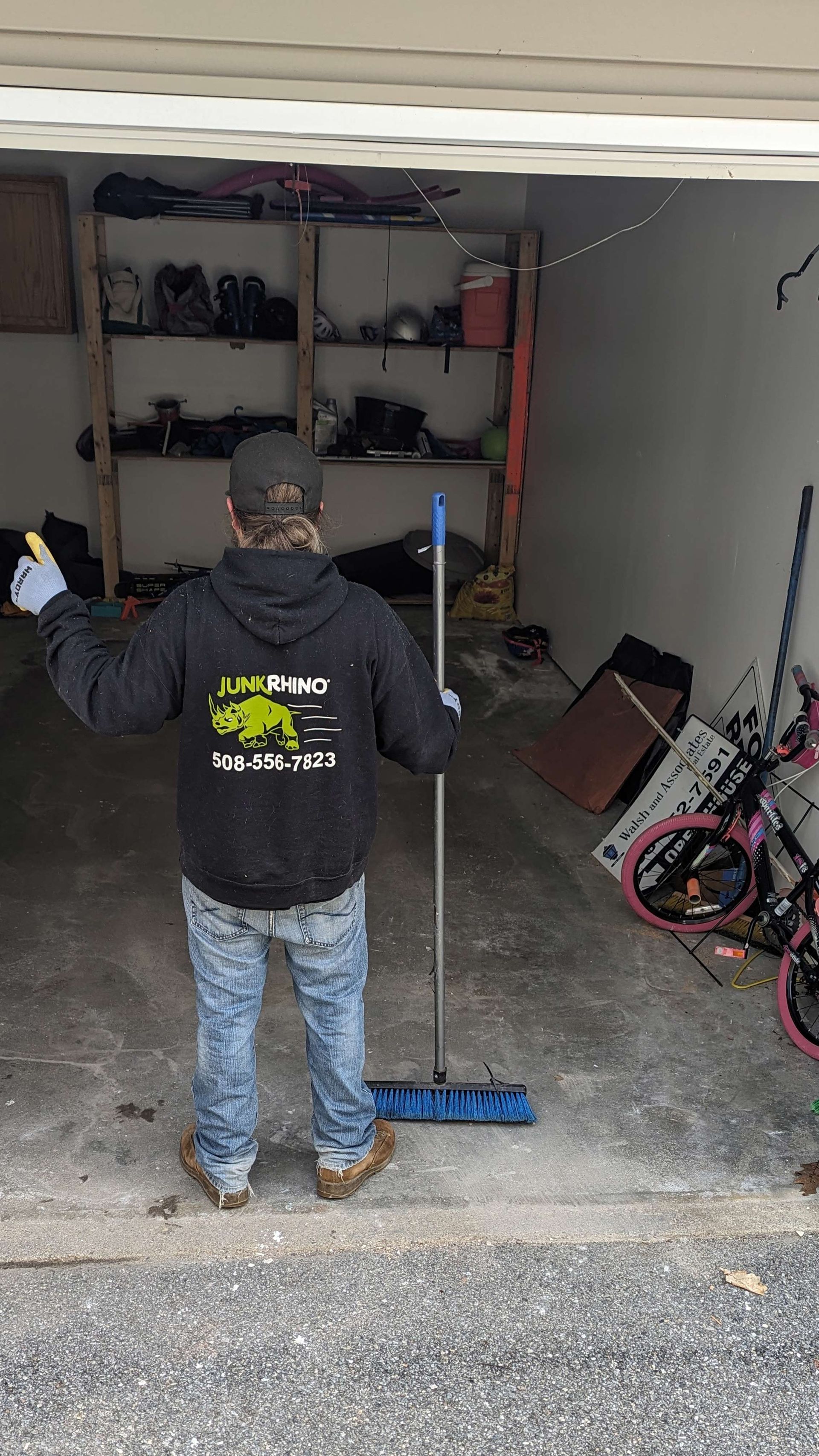 Person in a hoodie cleaning a garage with a mop. Shelves and bikes are visible.