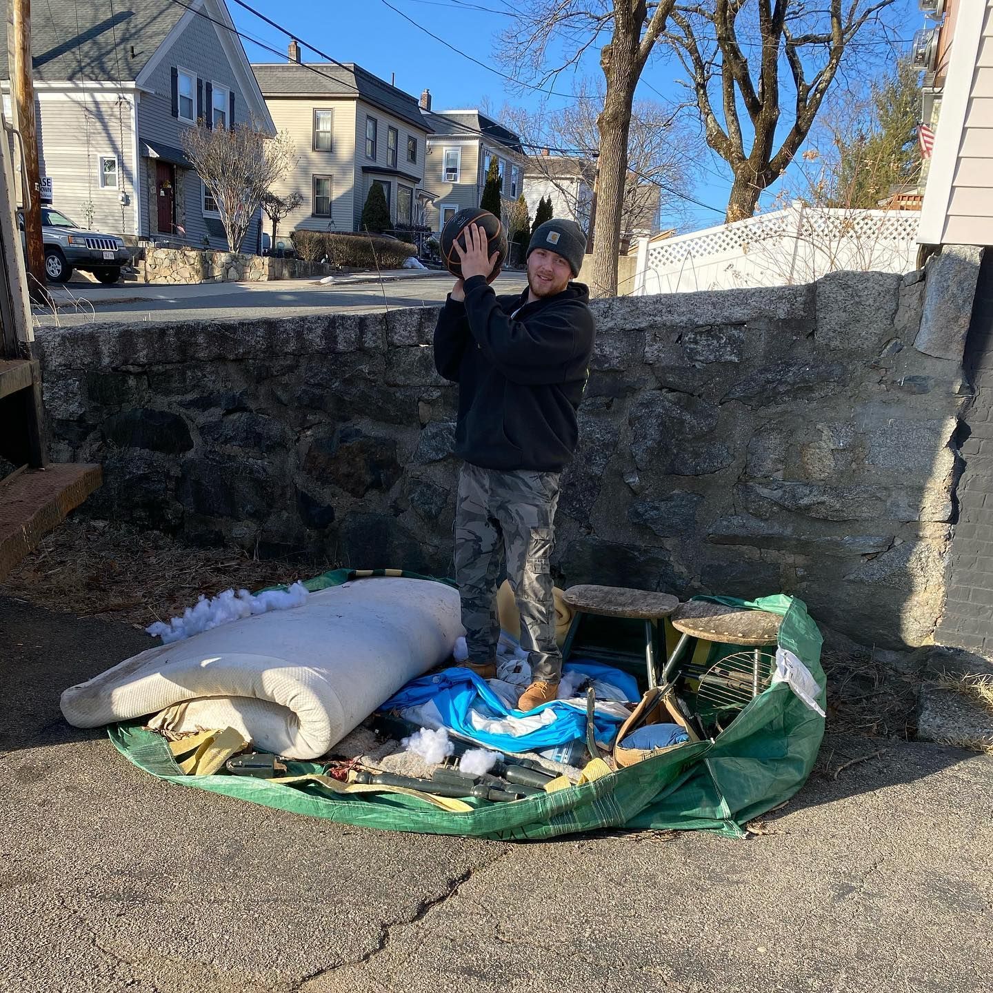 Man holding a ball above a pile of trash, likely cleaning up. Sunny day, urban setting.