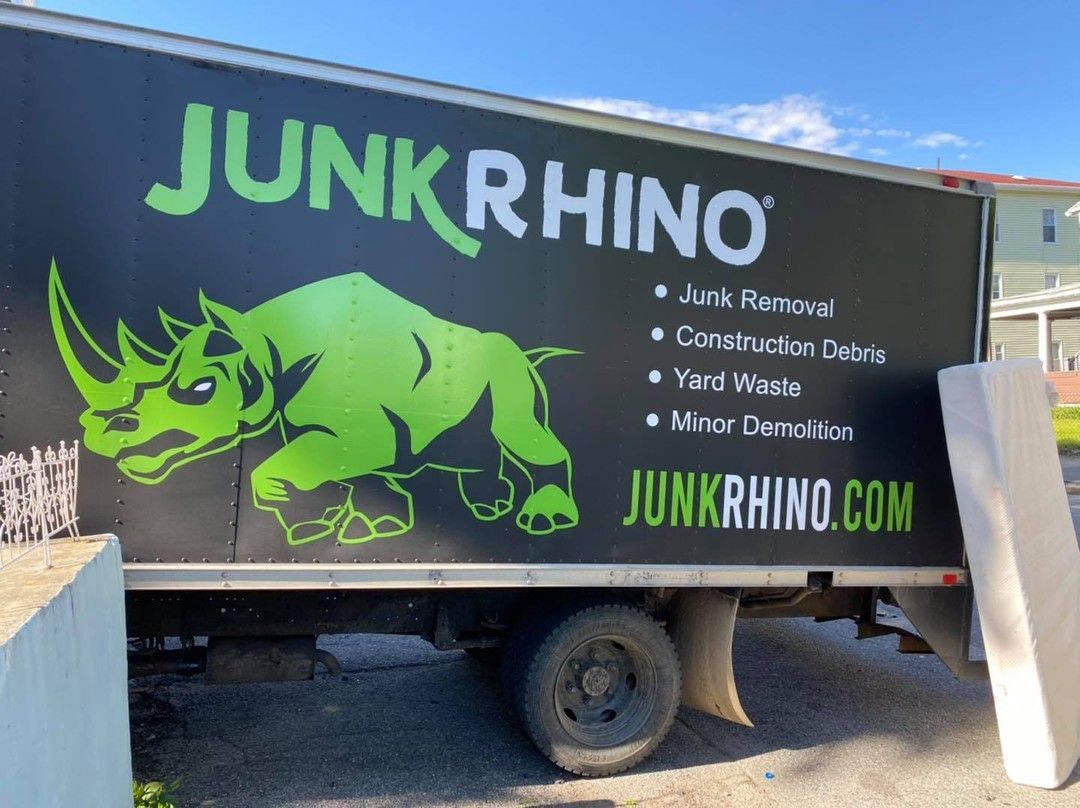 Junk Rhino truck with green rhino logo and services listed. Black truck, outdoors.