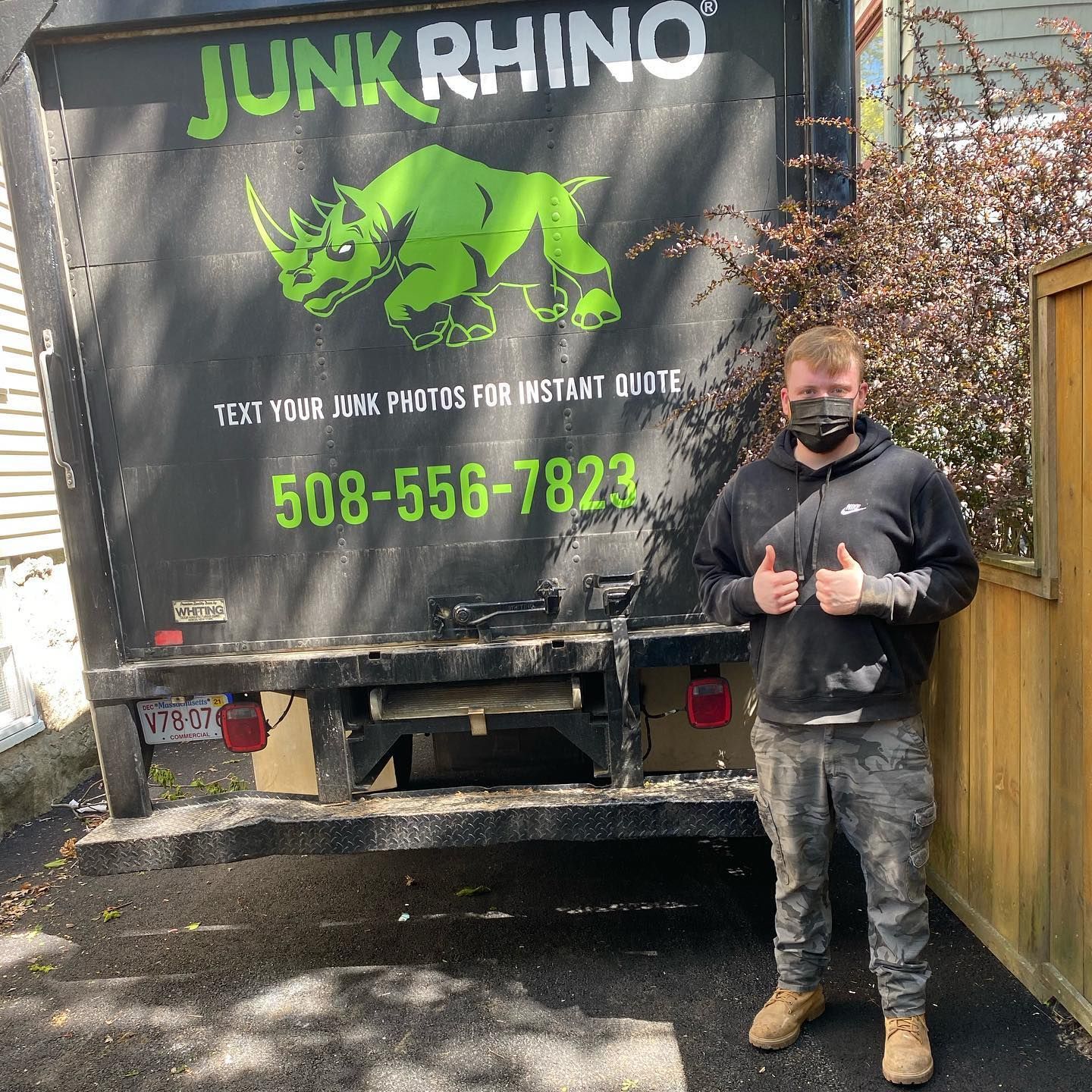 Man in black mask and dirty clothes, thumbs up by Junk Rhino truck with contact info.