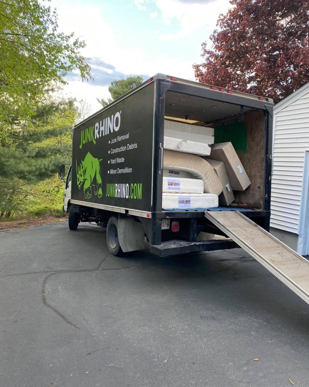 A Junk Rhino truck loaded with items on a driveway, ramp extended.