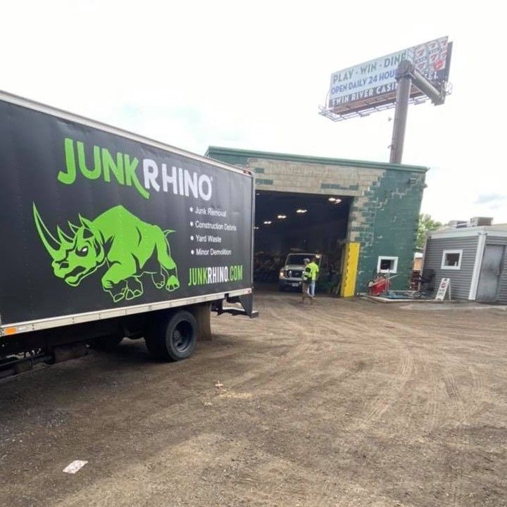 Junk Rhino truck parked outside a green building; a person in a vest stands nearby.