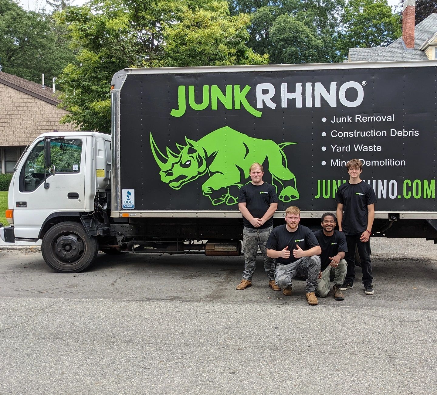 Four people pose in front of a Junk Rhino truck; the logo features a green rhino.