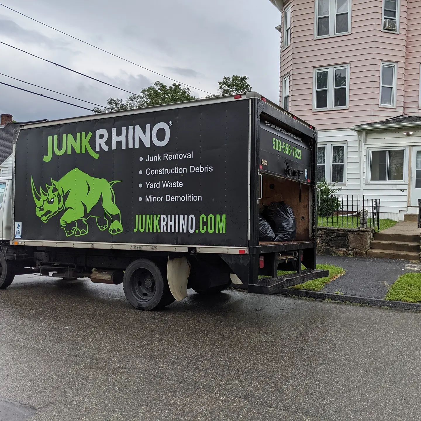 Junk removal truck parked in front of a house, its back door open with trash bags visible.