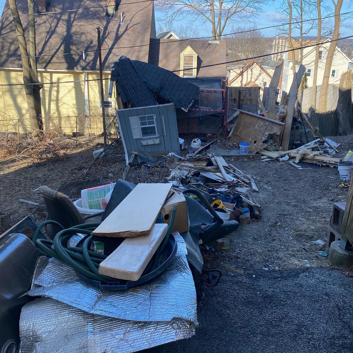 Backyard cluttered with debris, including wood, a shed, and various items. Sunny day.