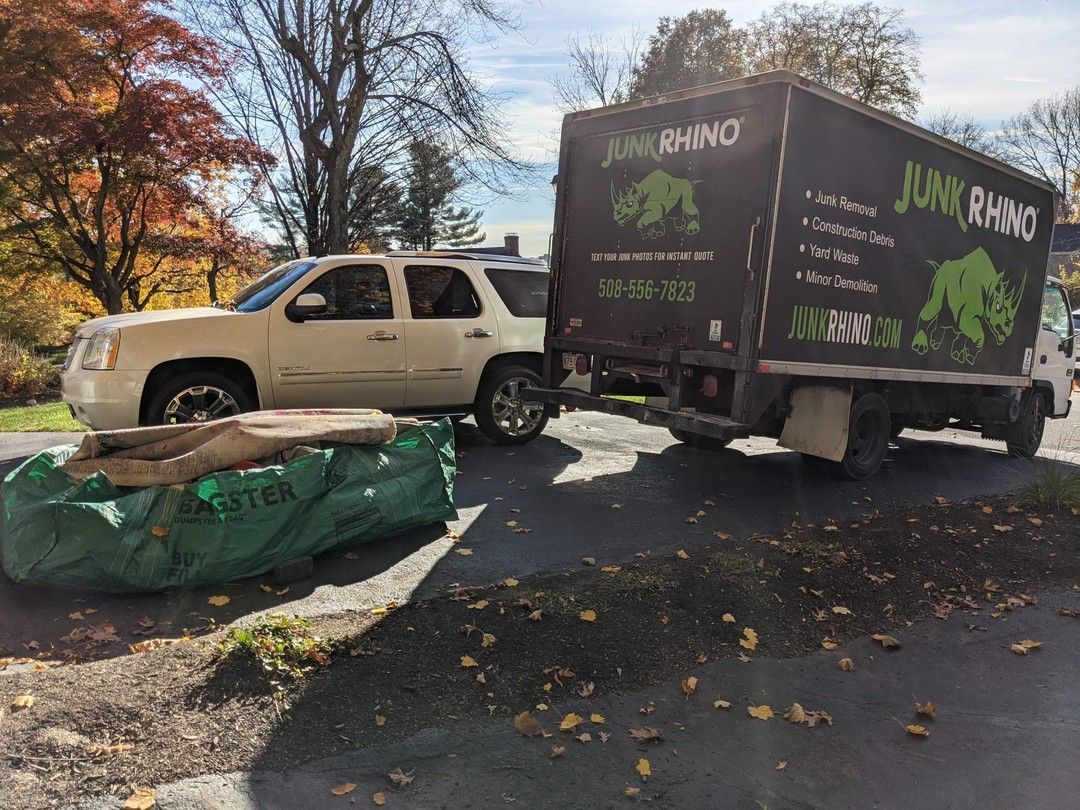 A white SUV and Junk Rhino truck parked on a driveway next to a green bag of debris.
