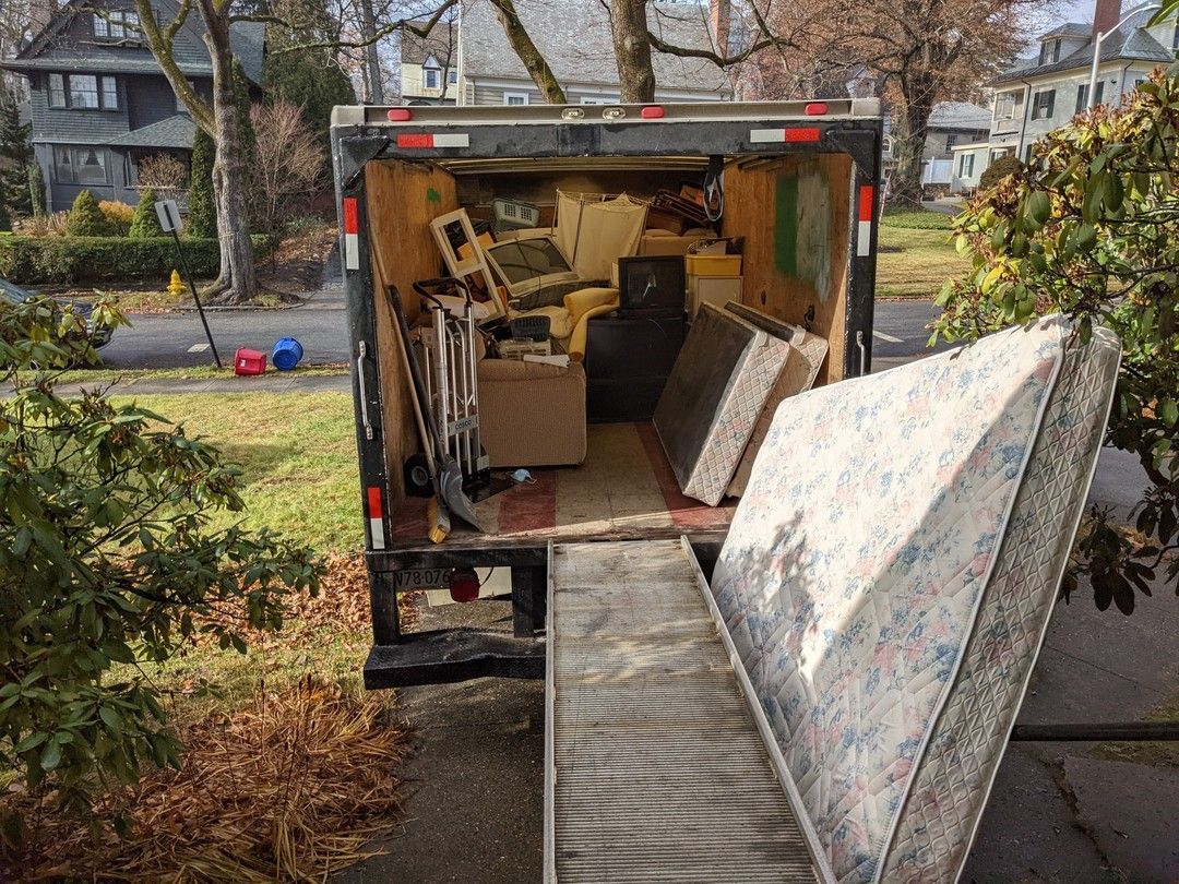 Open moving truck filled with furniture and other items, parked on a residential street.