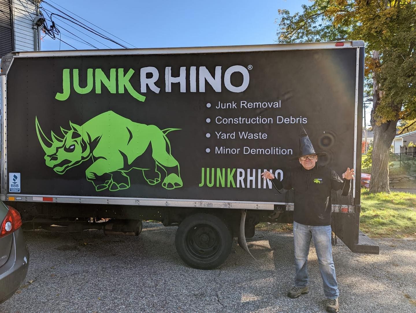 Person in front of a Junk Rhino truck; person is smiling with arms raised.