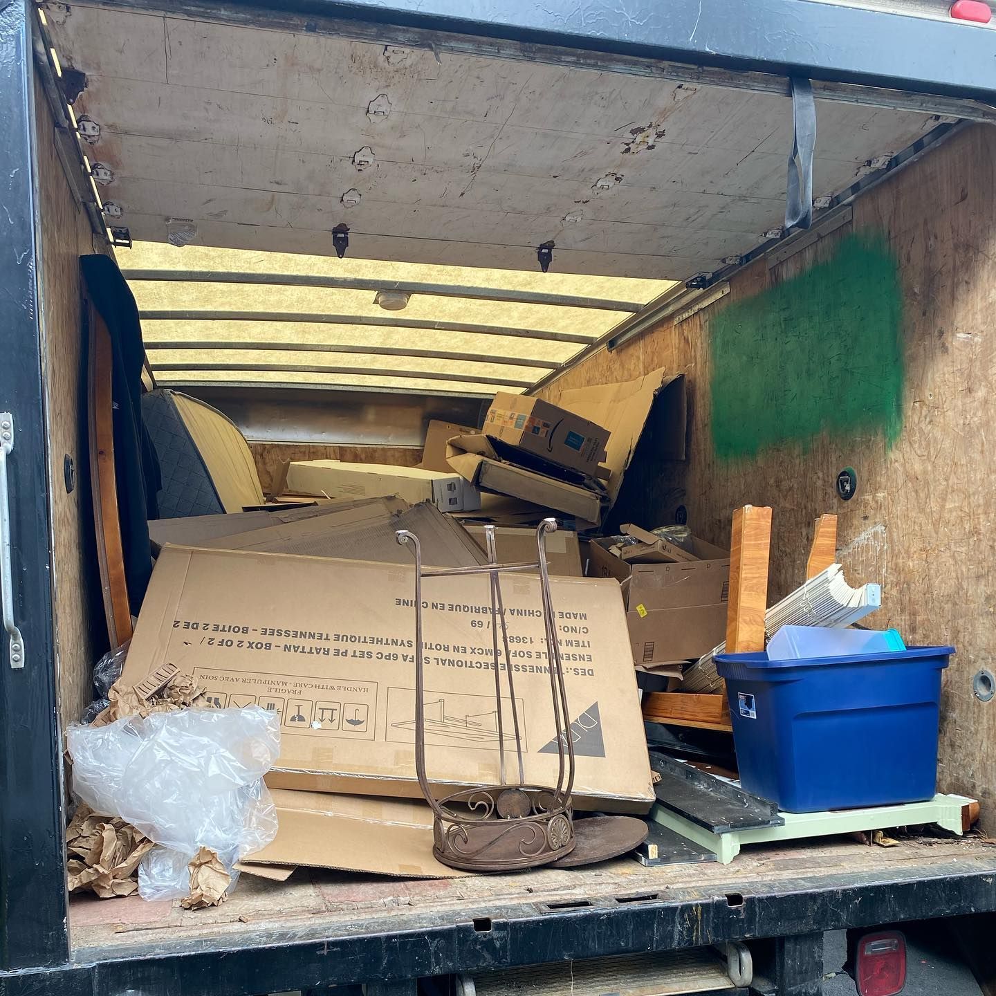 Inside a moving truck filled with cardboard boxes, furniture, and a blue bin.