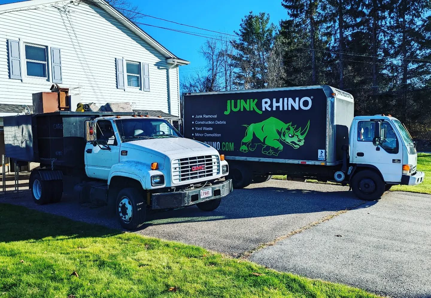 Two Junk Rhino trucks parked in a driveway. One is a white GMC truck, the other a white box truck.