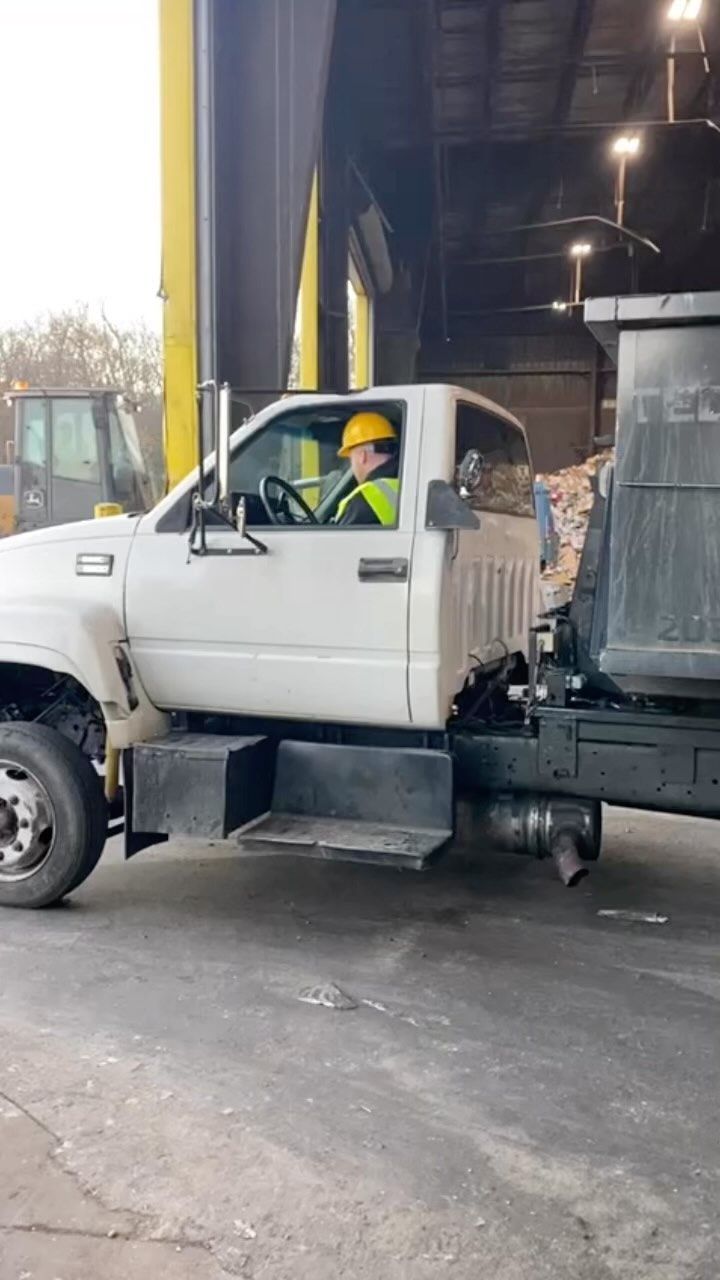 White dump truck with a person wearing a hard hat and safety vest, driving inside a building.