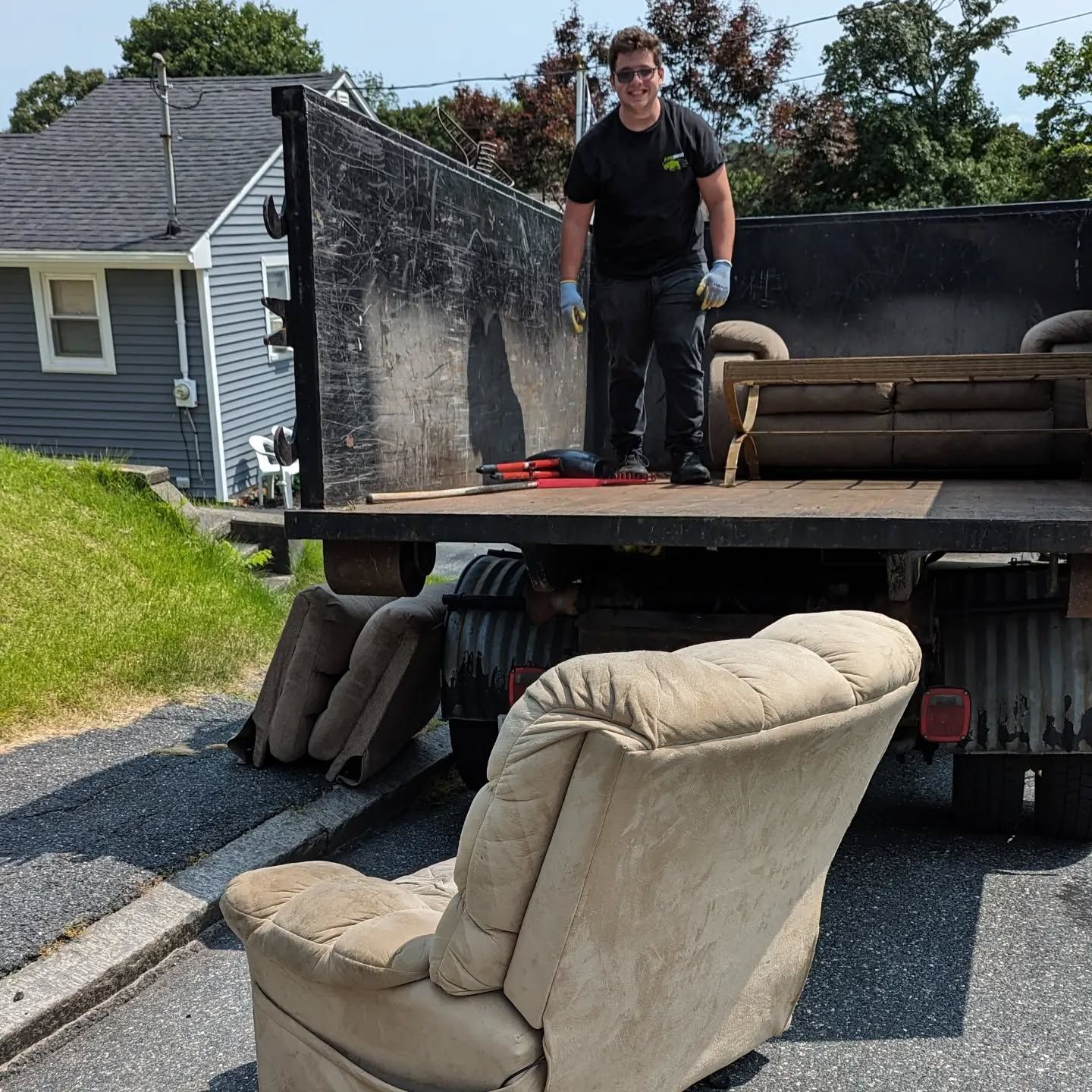 Man standing in truck bed loaded with furniture; chair in foreground.