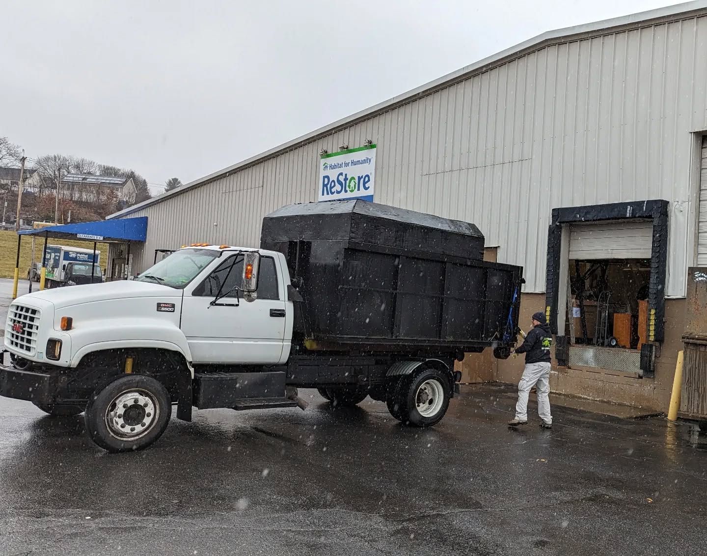 White truck with a black dumpster next to a ReStore loading dock, person unloading items.